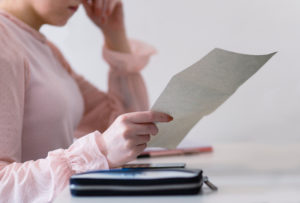 A woman holding and reading a bill and looking worried.